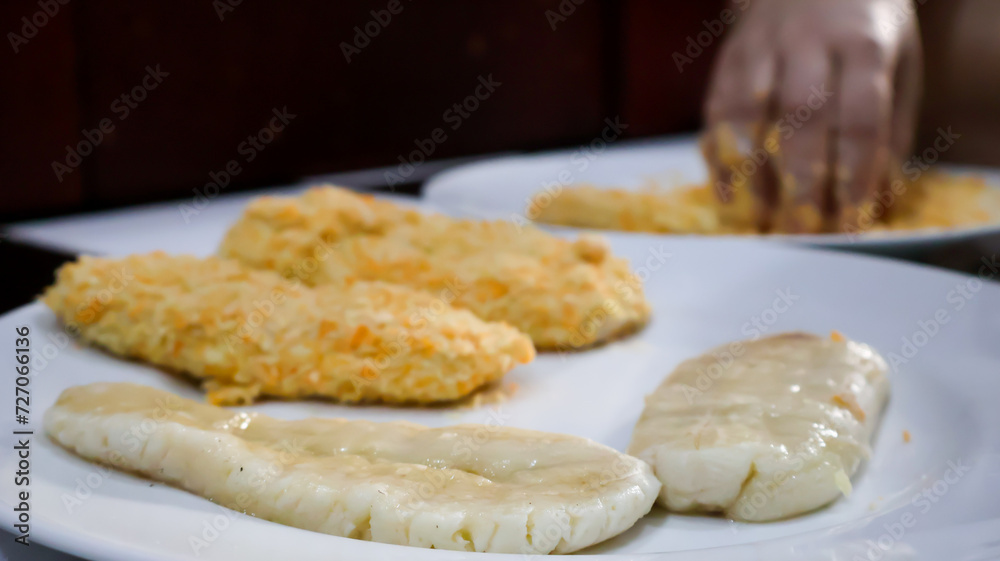 Wall mural Close-up of a woman making fried banana by coating the banana in golden bread crumb to then be fried. Ideal for food blogs, cooking concepts, food enthusiasts, and cooking-themed designs. 