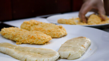Close-up of a woman making fried banana by coating the banana in golden bread crumb to then be fried. Ideal for food blogs, cooking concepts, food enthusiasts, and cooking-themed designs. 