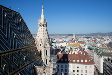 The high spire of the church is in the Gothic style. High dome of gray color in cat style. Panorama of the capital of Austria, Vienna. Stylish colored roof tiles. - Powered by Adobe