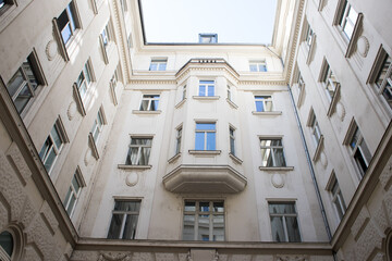 Obraz premium Inner courtyard of a five-story building. White facade of a house with loggias. Convex elements in the facade of a building. Circular courtyard. Clear sky through the walls of the house.