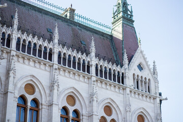 Fototapeta na wymiar Hungarian Parliament in Budapest. Details of the facade of the Parliament in Hungary. Gothic style in architecture. Angular buildings. Burgundy roof of the building. Windows of unusual shape.