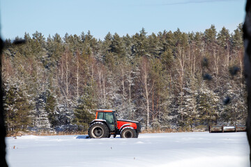 Red tractor in winter on snow with forest in background