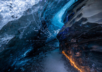 Blue glacial ice cave illuminated by orange light in Iceland