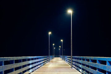 Lampposts along pier going into night darkness above sea symbolize serene scene of calmness cold winter night, minimalist geometry of pier in calming night sky, pier to open sea without people