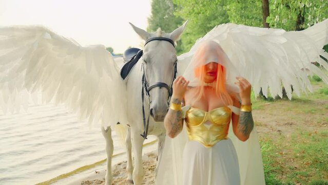 Art video real people Fantasy woman with horse. Lady warrior queen, pet wings pegasus animal. Greek style fairy tale girl sexy face elf takes off hood walking by sea beach summer nature sky tree. 4k