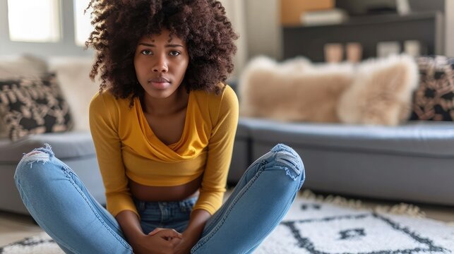 Black Lady Suffering From Menstrual Pain, Feeling Sick To Her Stomach, Touching Belly, Having Abdominal Cramps During Period, Sitting On Floor Near Couch At Home