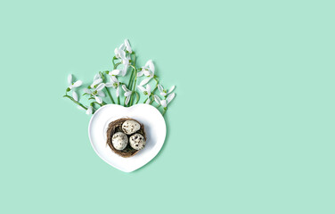 snowdrops flowers, heart plate with  eggs in nest on green background. symbol of spring season....