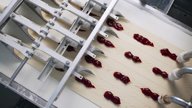 The process of adding berry jam to bun dough at a confectionery factory. Close-up of products filled with jam and transported along a conveyor belt. The concept of automated technological equipment of