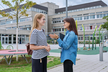 Talking teacher and teenage schoolgirl outdoor, school building background