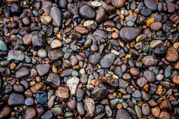 Abstract river colorful pebble stones background. ?attern of wet rocks gracefully arranged. Each stone glistens in the gentle water, creating an intricate mosaic of earthy colors and textures