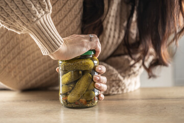 A woman tries to force open a jam jar with cucumbers - obrazy, fototapety, plakaty