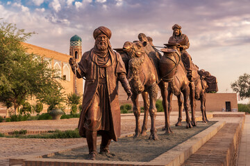 Sculpture of camel carrying goods and man in Uzbek dress in front of city walls, Khiva, Uzbekistan