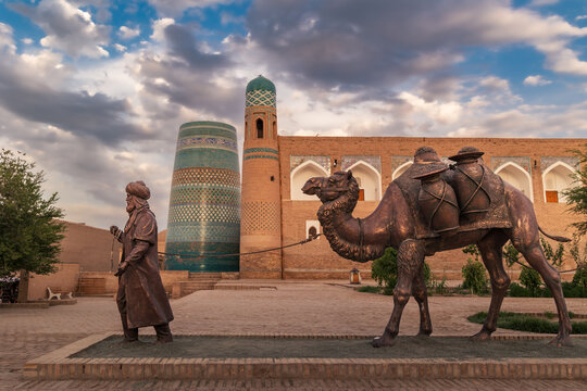 Sculpture of camel carrying goods and man in Uzbek dress in front of city walls, Khiva, Uzbekistan