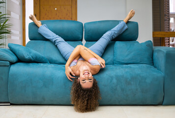 Cheerful woman lying upside down on sofa at home