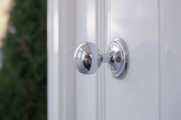 A sleek, modern, chrome doorknob on a white painted door. Hamptons style architecture. 
