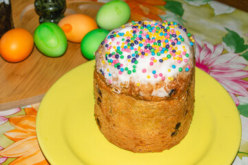 Easter cake on a wooden board. Christians celebrate Easter. Colorful Easter eggs. A cake with colorful sweet sprinkles. Religious holidays of Christians. A festive cake and eggs on the table.