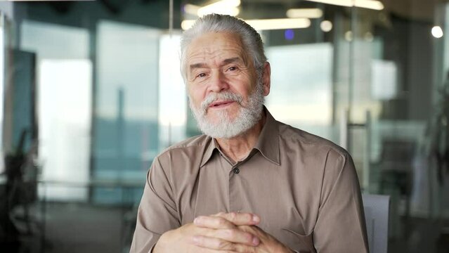 Senior gray haired businessman watching video call online conference looking at camera at laptop computer screen sitting in office. Elderly male listening remote meeting, talking with business partner