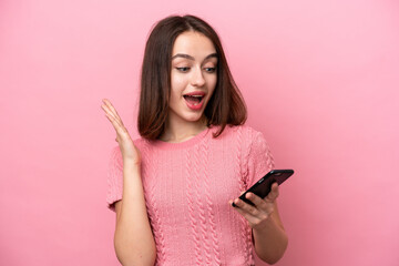 Young Ukrainian woman isolated on pink background looking at the camera while using the mobile with...