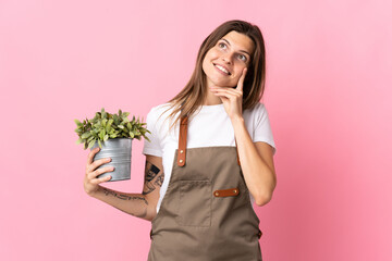 Gardener woman holding a plant isolated on pink background thinking an idea while looking up