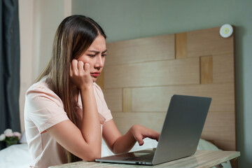 Frustrated Asian woman experiences moment of stress while working on  laptop in bedroom, embodying...