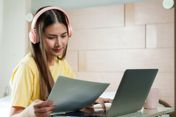Focused and poised, young woman with headphones examines document, multitasking in work from home....