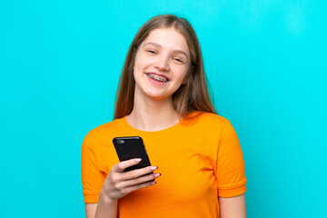 Teenager Russian girl isolated on blue background using mobile phone