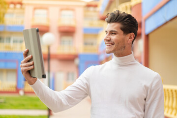 Young caucasian man holding a tablet at outdoors with happy expression