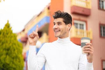 Young caucasian man holding a take away coffee at outdoors intending to realizes the solution while lifting a finger up