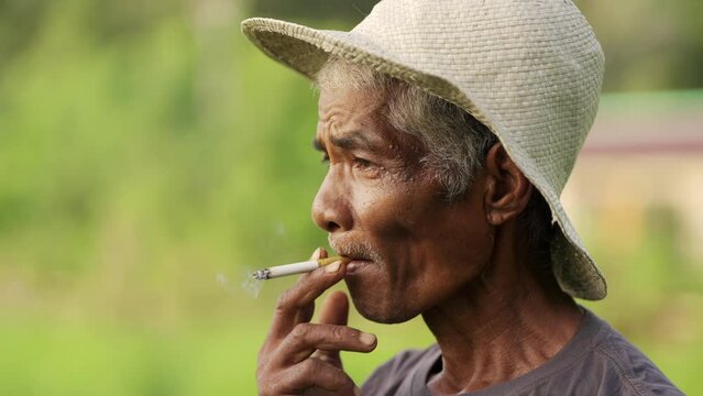 senior asian farmer smoker in straw hat on field, slow motion cigarette smoke