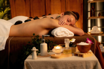 Hot stone massage at spa salon in luxury resort with warm candle light, blissful couple customer...