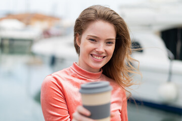 Young redhead woman holding a take away coffee at outdoors with happy expression