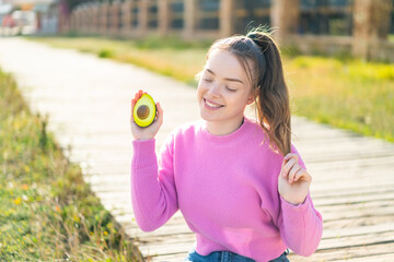 Young pretty girl at outdoors holding an avocado with happy expression