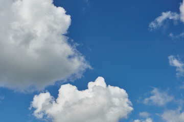 White fluffy clouds in the sky. Blue sky and cloud cover on a sunny summer day. Empty background, copy space