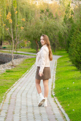 A young smiling girl walking in an autumn park in a good mood. Teenage girl, portrait against a background of nature. Fashion style trend.