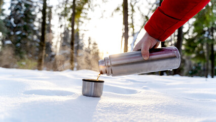 A tourist pours tea from a thermos in a winter forest