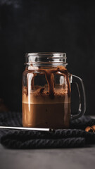 Ice cold coffee with chocolate in a glass jar on a dark background