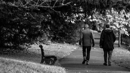 In monochrome, two men stroll along a path, a bench nearby, embodying the timeless camaraderie...
