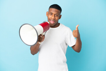 Young latin man isolated on blue background holding a megaphone with thumb up