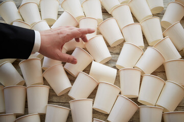 White paper cups scattered on the table in warm sunlight and a businessman’s hand reaching for...