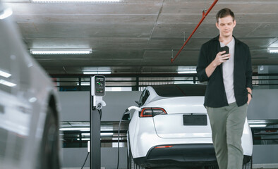 Young man travel with EV electric car to shopping center parking lot charging in downtown city...