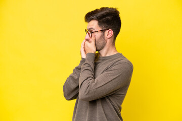 Young caucasian man isolated on yellow background covering mouth and looking to the side