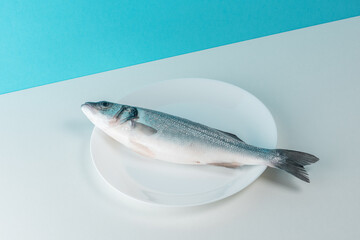 Raw fresh seabass fish on a white plate. Minimal food concept.