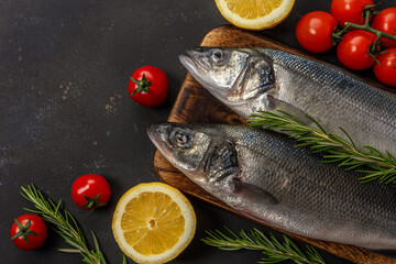 Two fresh seabass fishes with rosemary and vegetables on black table.