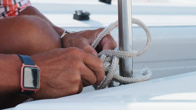 Sailor illustrates knot-crafting finesse on yacht. Skilled yachtsman offers secure and versatile method for mooring sailboat