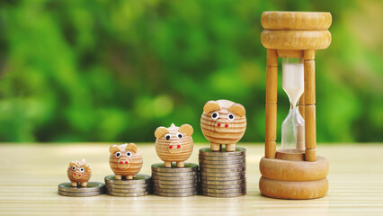 Hourglass and Rows of money coins stacks as step stair with wooden piggy bank on wooden table with...