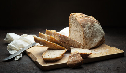 Traditional bread cut into slices. Loaf of bread with knife and cutting board on dark background, close-up, space for text.