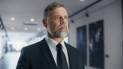 Portrait of a Confident Businessman Walking To His Office in a Bright Business Center Skyscraper: Successful Senior Manager with Serious Face Expression Walking to Workplace in the Morning.