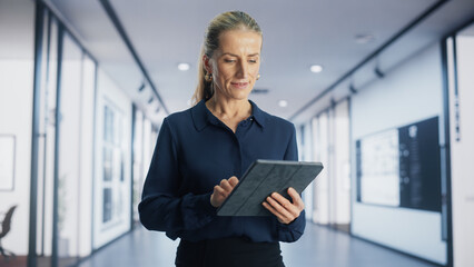 Portrait of Caucasian Female Project Manager Using a Tablet Computer and Walking in a Corridor of a Modern Office Building. Successful Businesswoman Working in an International Ecommerce Company - obrazy, fototapety, plakaty