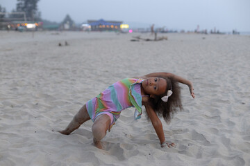 6-7 years old African-American girl is doing sports on summer day on beach. Children's gymnastics. 