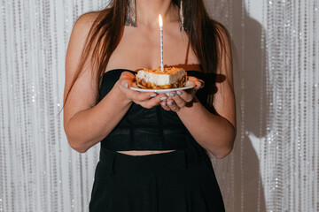 A girl in a black dress is holding a cake with a candle for her birthday. Close-up photo